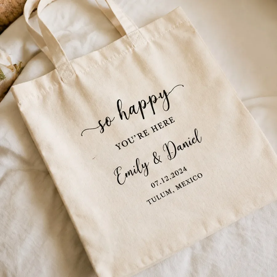 A printed cotton welcome tote lying on cream linen, its names and date facing up
